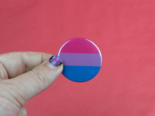 Hand holding a round bisexual pride flag against a red background