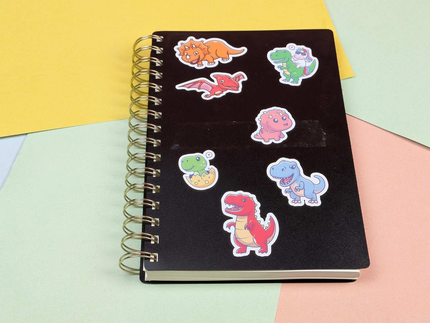 Black notebook with colorful dinosaur stickers on a multicolored background