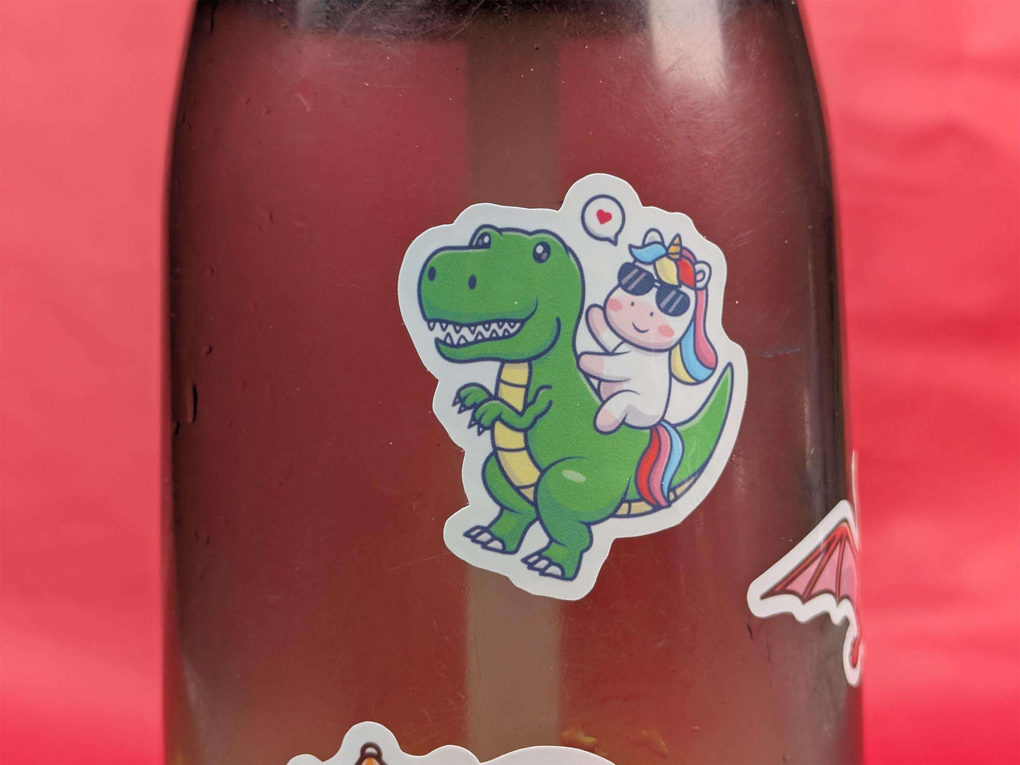 Bottle with a green dinosaur and unicorn sticker on a red background