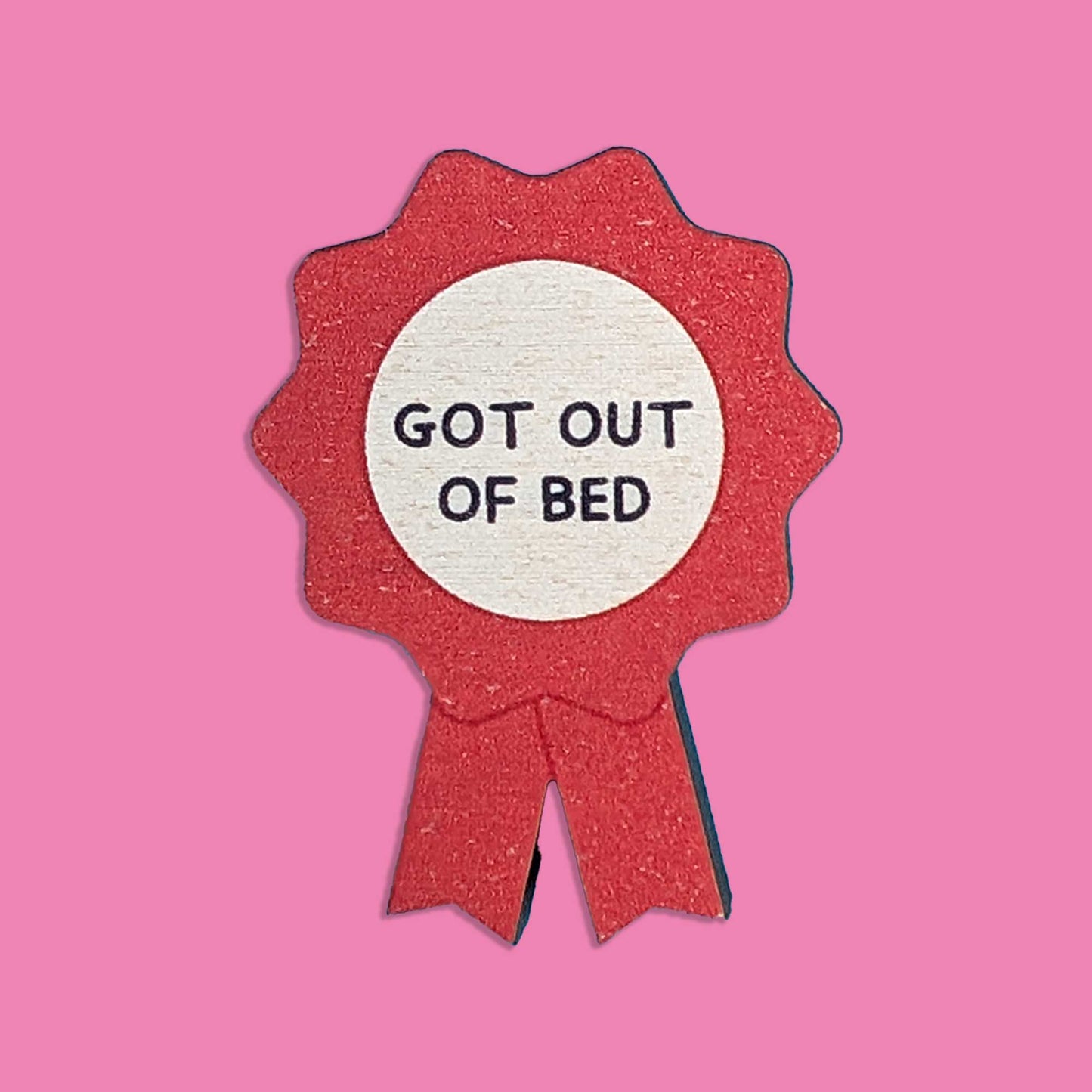 A red glitter ribbon award badge with a white center and the text 'GOT OUT OF BED' in black lettering, shown on a solid pink background.