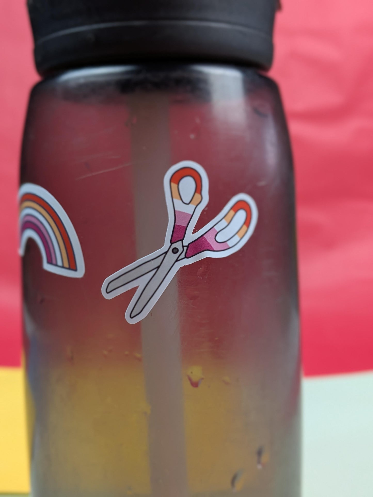 Bottle with a colorful sticker of scissors and a rainbow on a red background