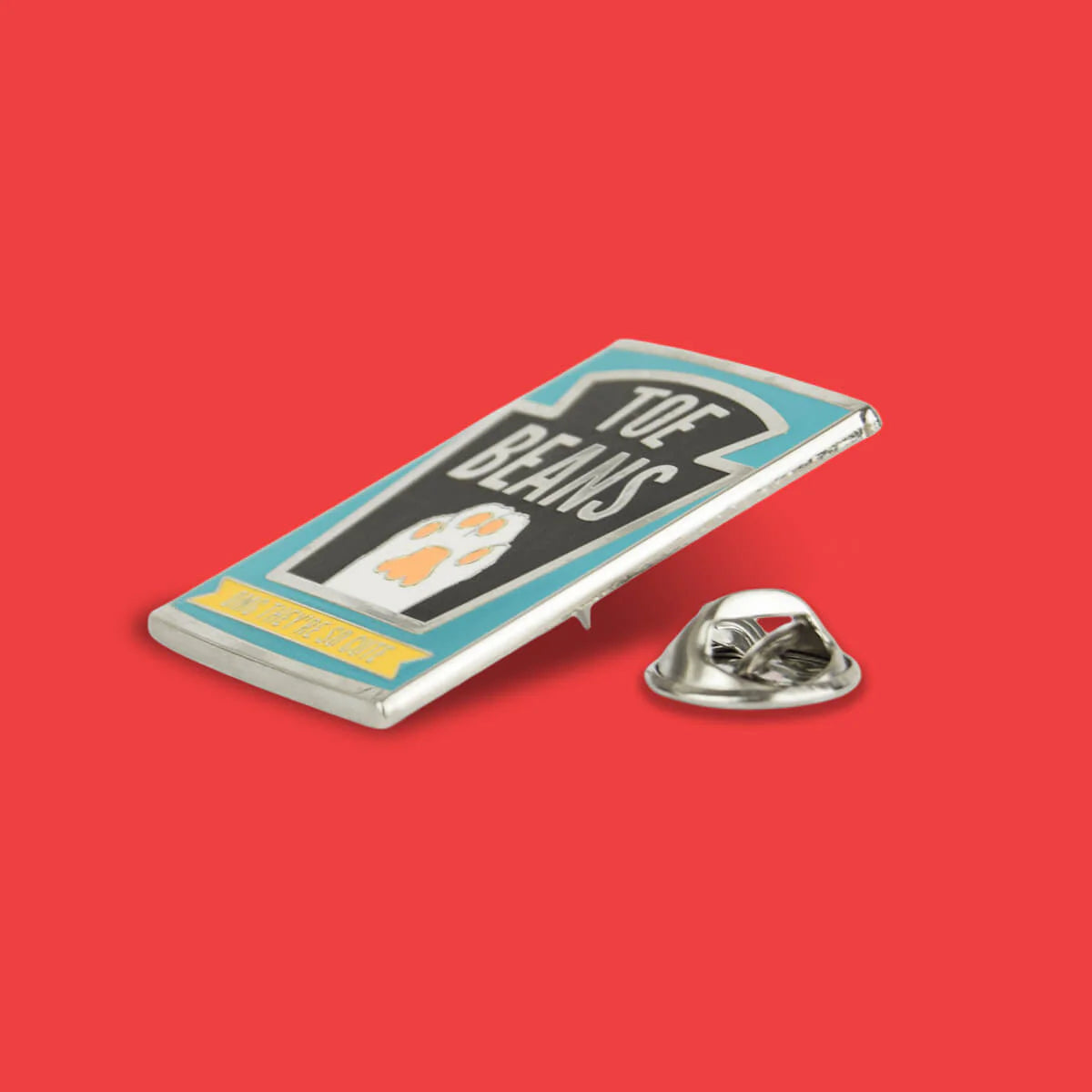Metallic pin with 'Toe Beans' design on a red background