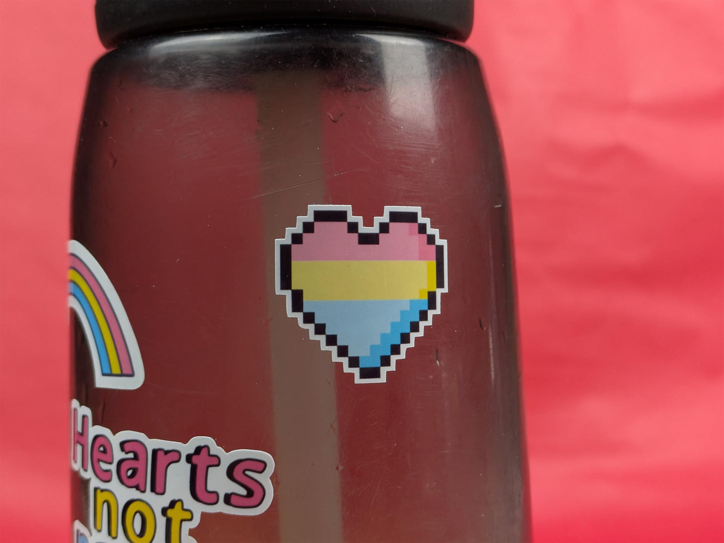 water bottle with pixelated heart and rainbow sticker on a red background