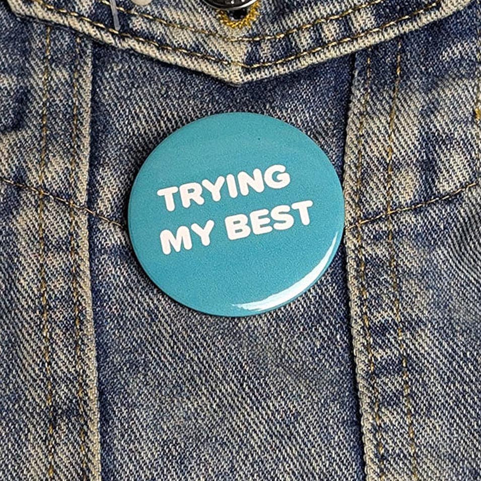 Blue button with 'TRYING MY BEST' text on a denim jacket