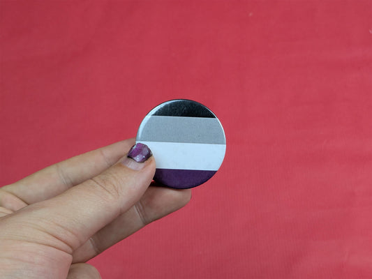 Hand holding a round asexual flag badge against a red background
