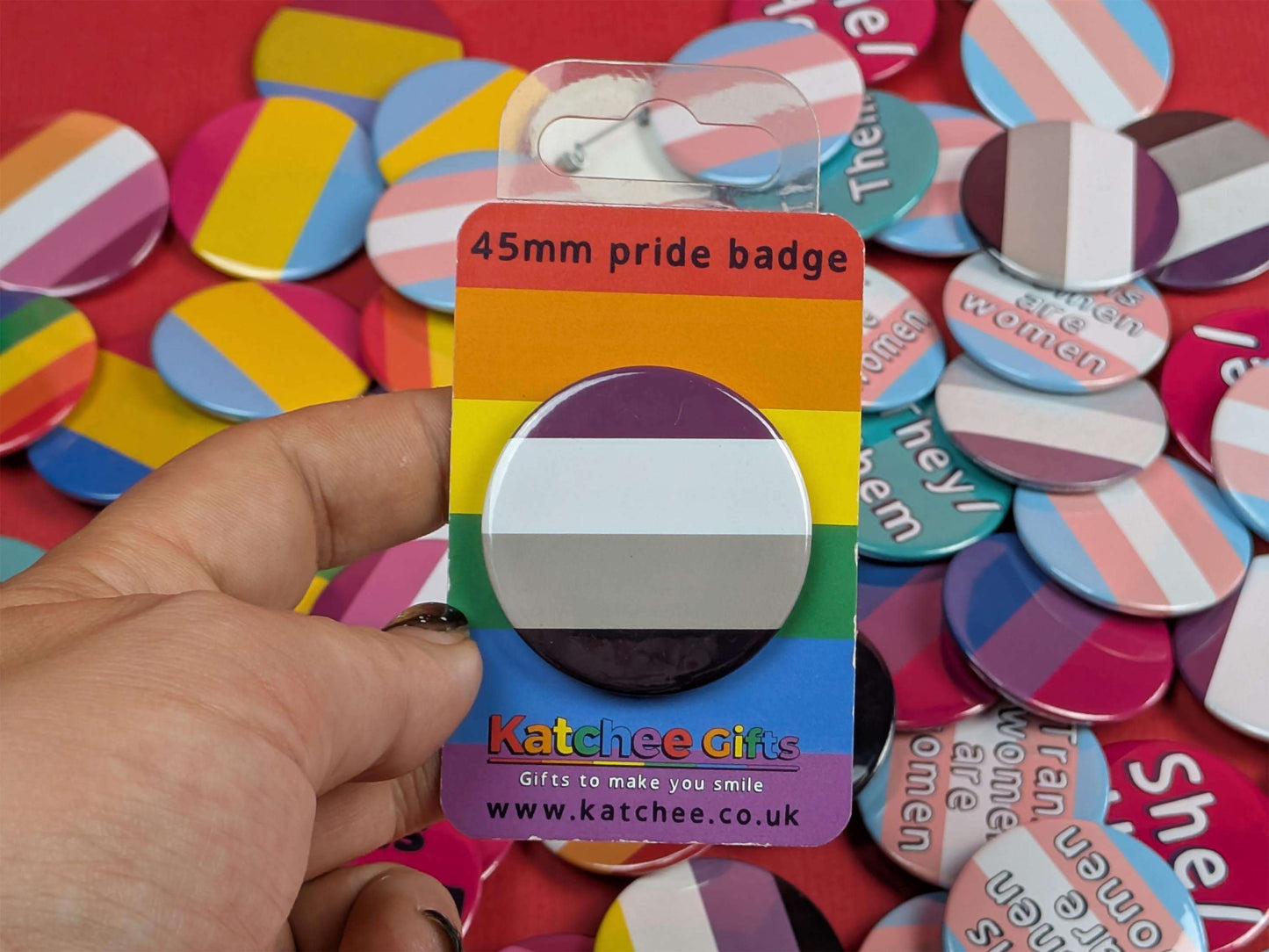 45mm pride badge in a rainbow card with a hand holding it, surrounded by various buttons.