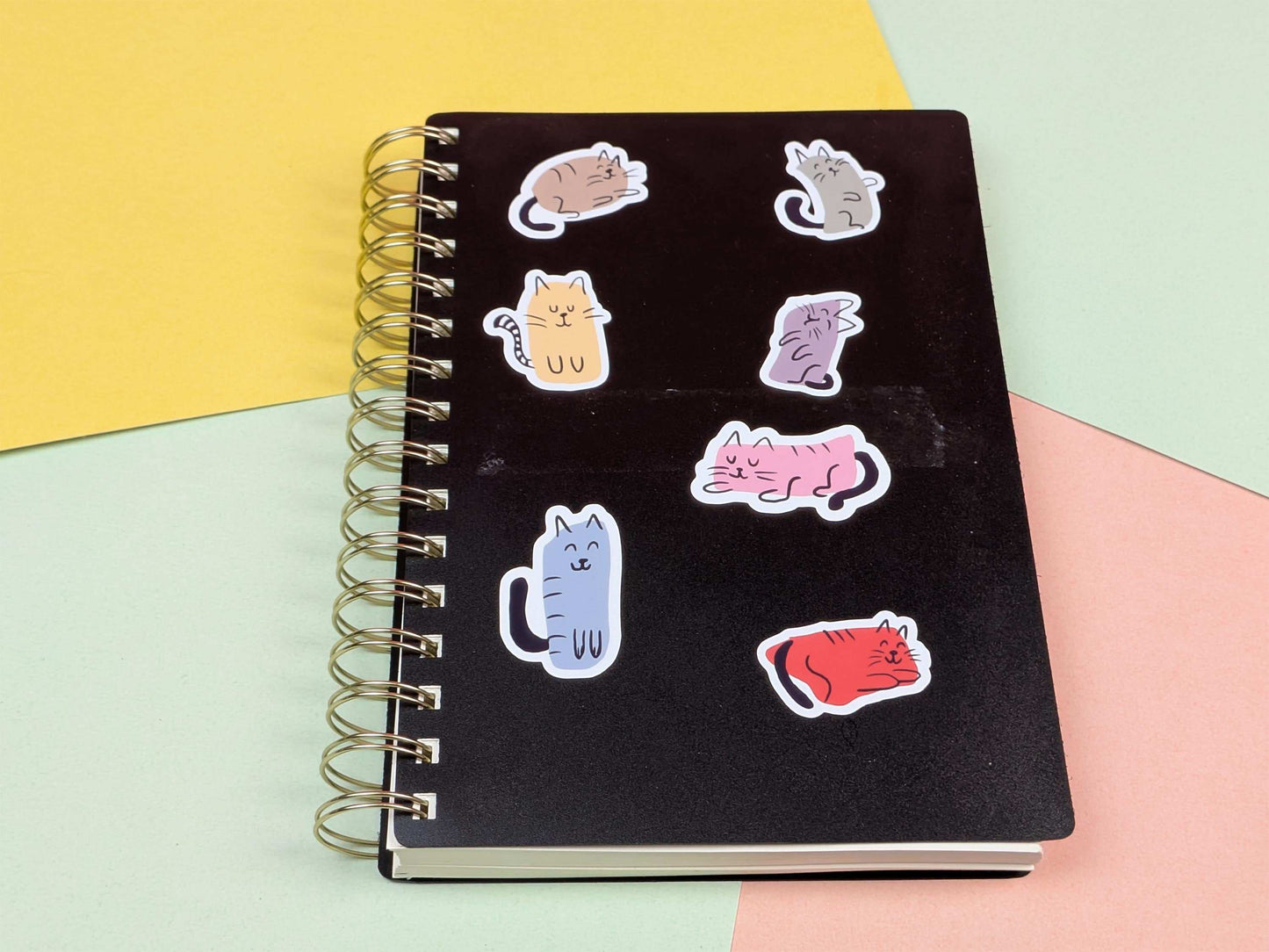 Black notebook with colorful cat-shaped stickers on a multicolored background