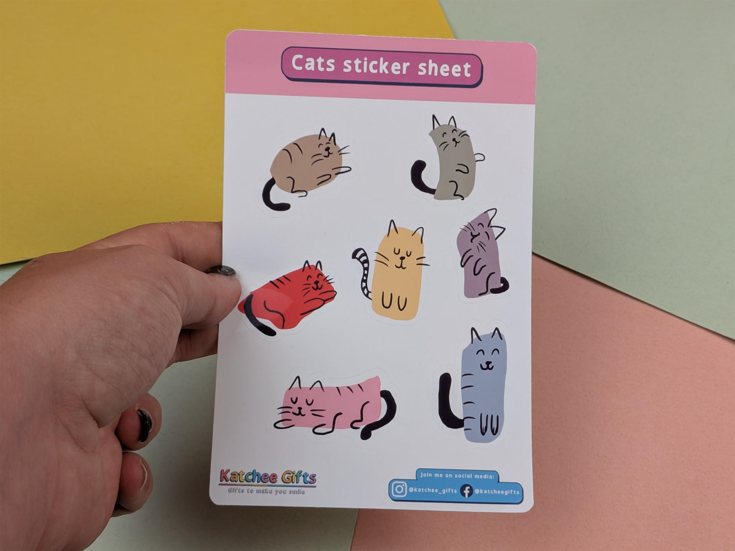 Sheet of cat stickers held by a hand against a colourful background