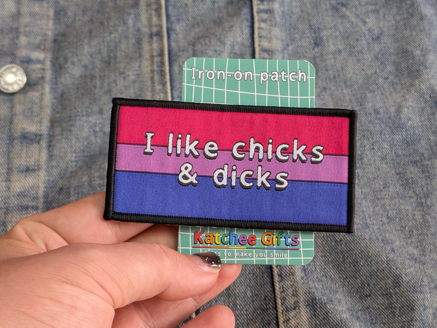 Iron-on patch with rainbow design and text held against a denim background