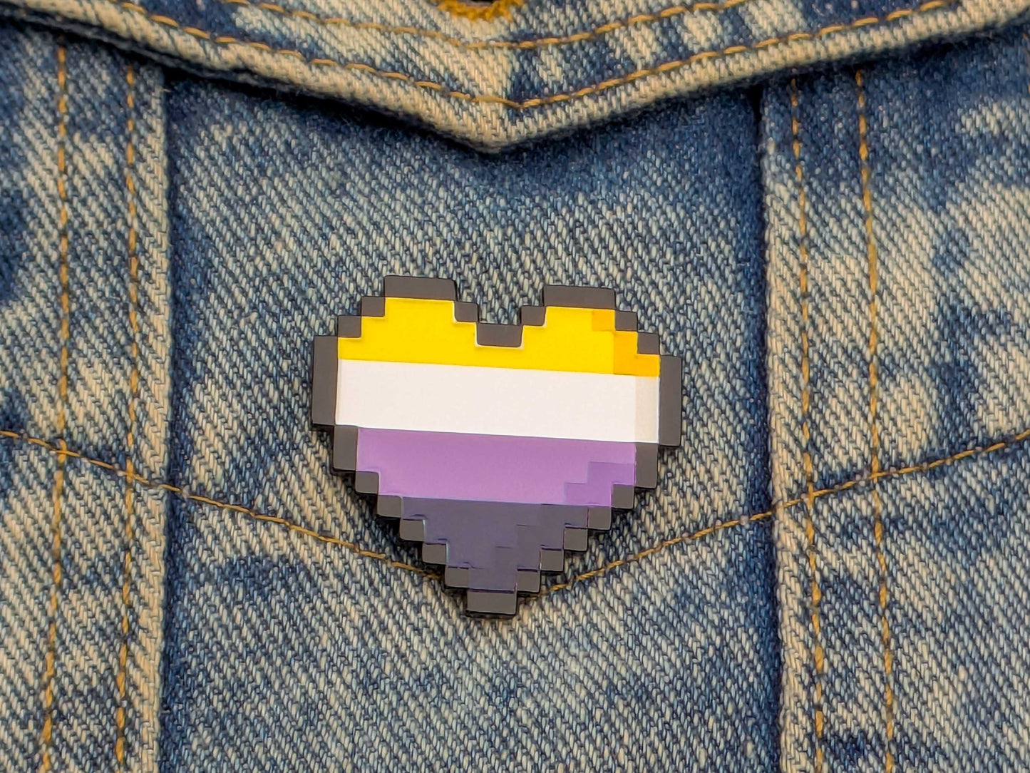 Pixelated heart-shaped pin with a non binary flag design on denim fabric