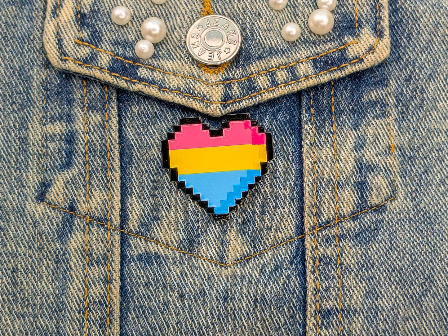 Pixelated heart-shaped pin with pansexual flag colors on a denim jacket.