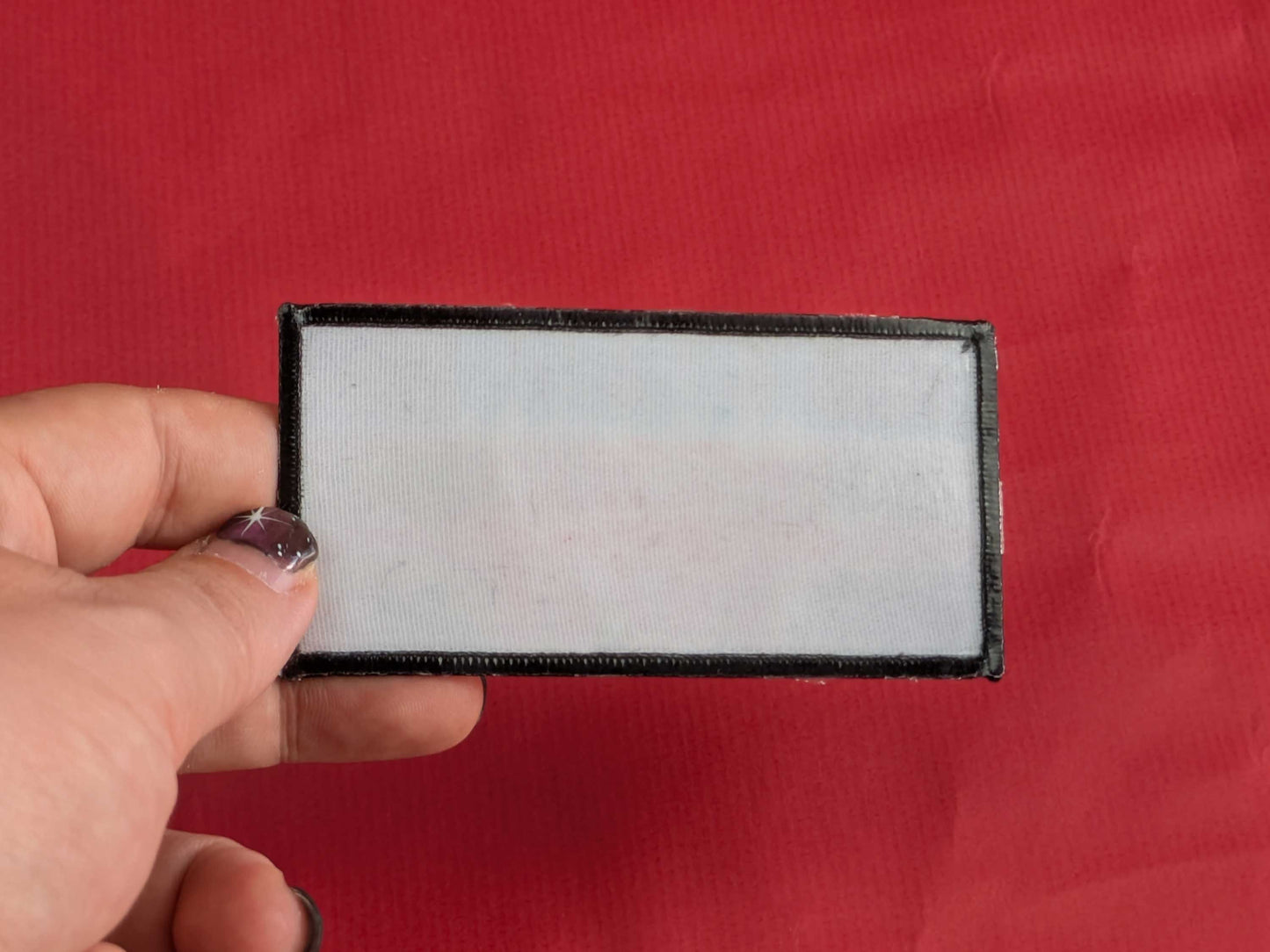 The back of an iron-on patch held by a hand against a red background