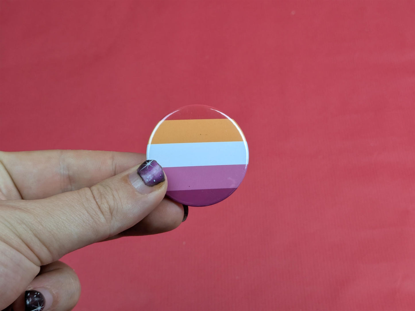 Hand holding a circular badge with the lesbian flag against a red background