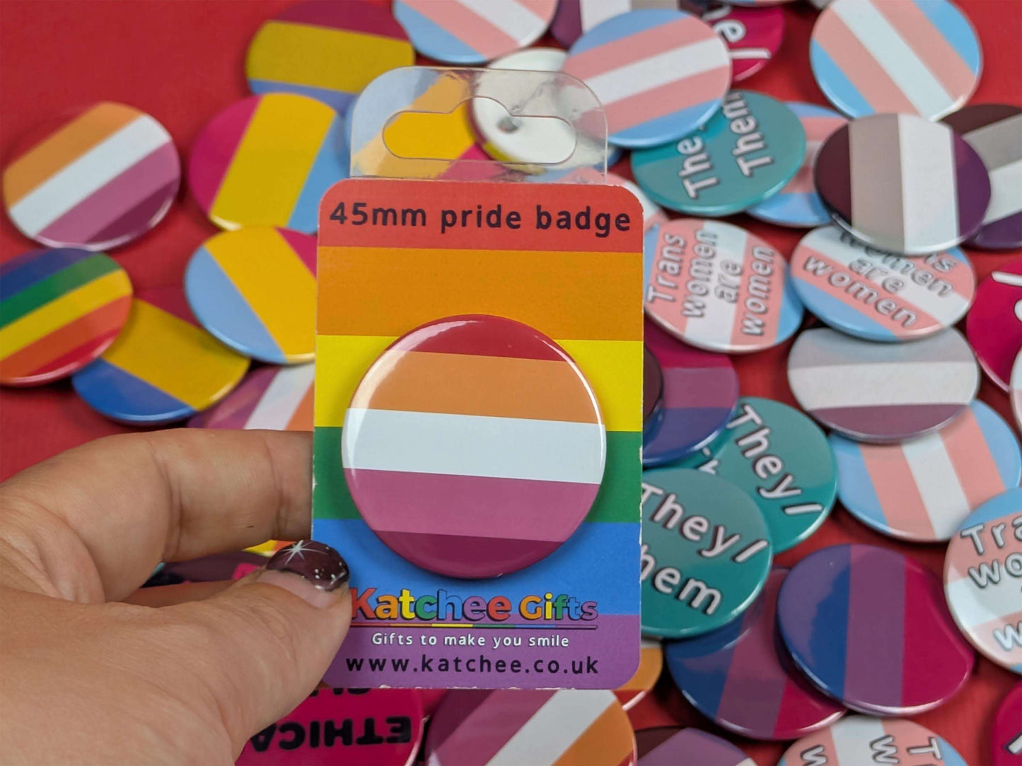 Packaged lesbian pride badge with a hand holding it against a background of various buttons.
