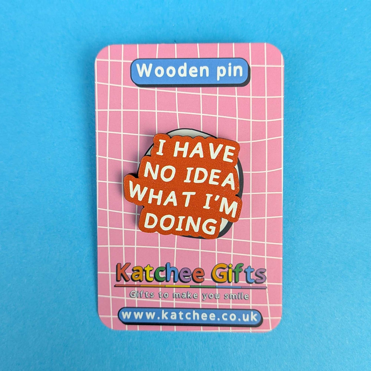 A wooden pin displayed on its pink backing card. The pin features a brown wooden base with layered orange, red, and yellow speech-bubble shapes containing the text 'I HAVE NO IDEA WHAT I'M DOING' in white.