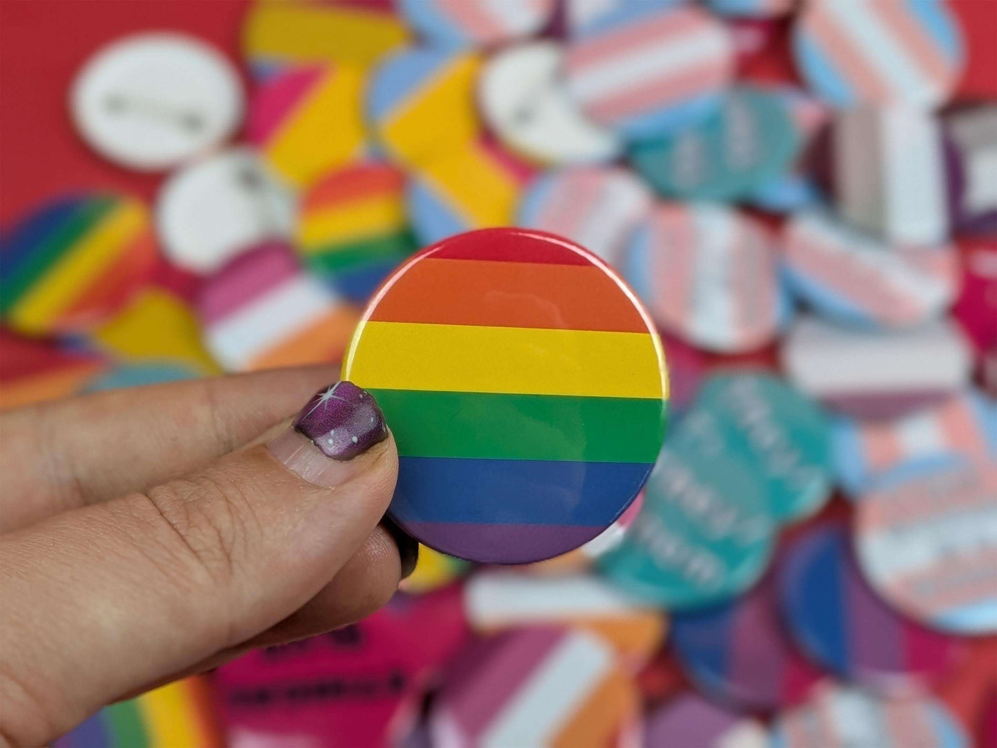 Hand holding a rainbow button badge with a colorful background of buttons.