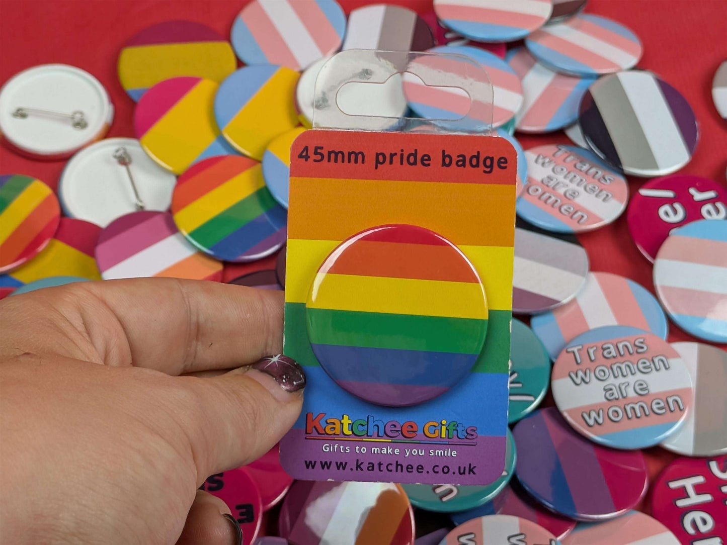 Rainbow pride badge in packaging held by a hand with a background of various buttons.