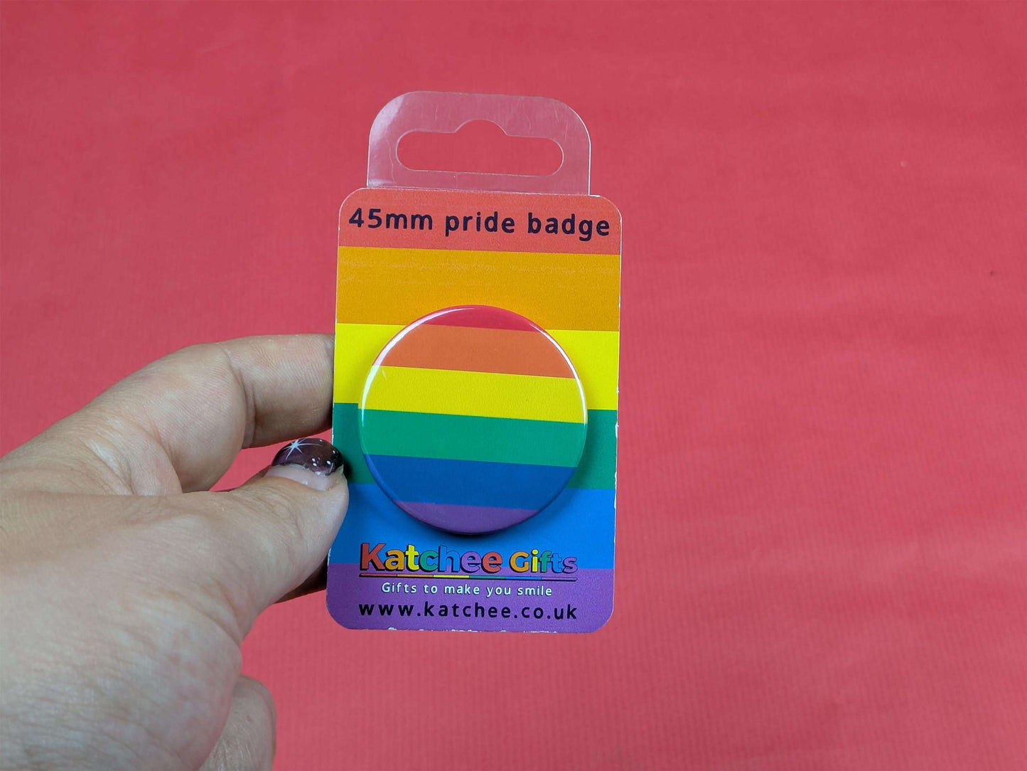 Rainbow pride badge on a clear card held by a hand against a red background