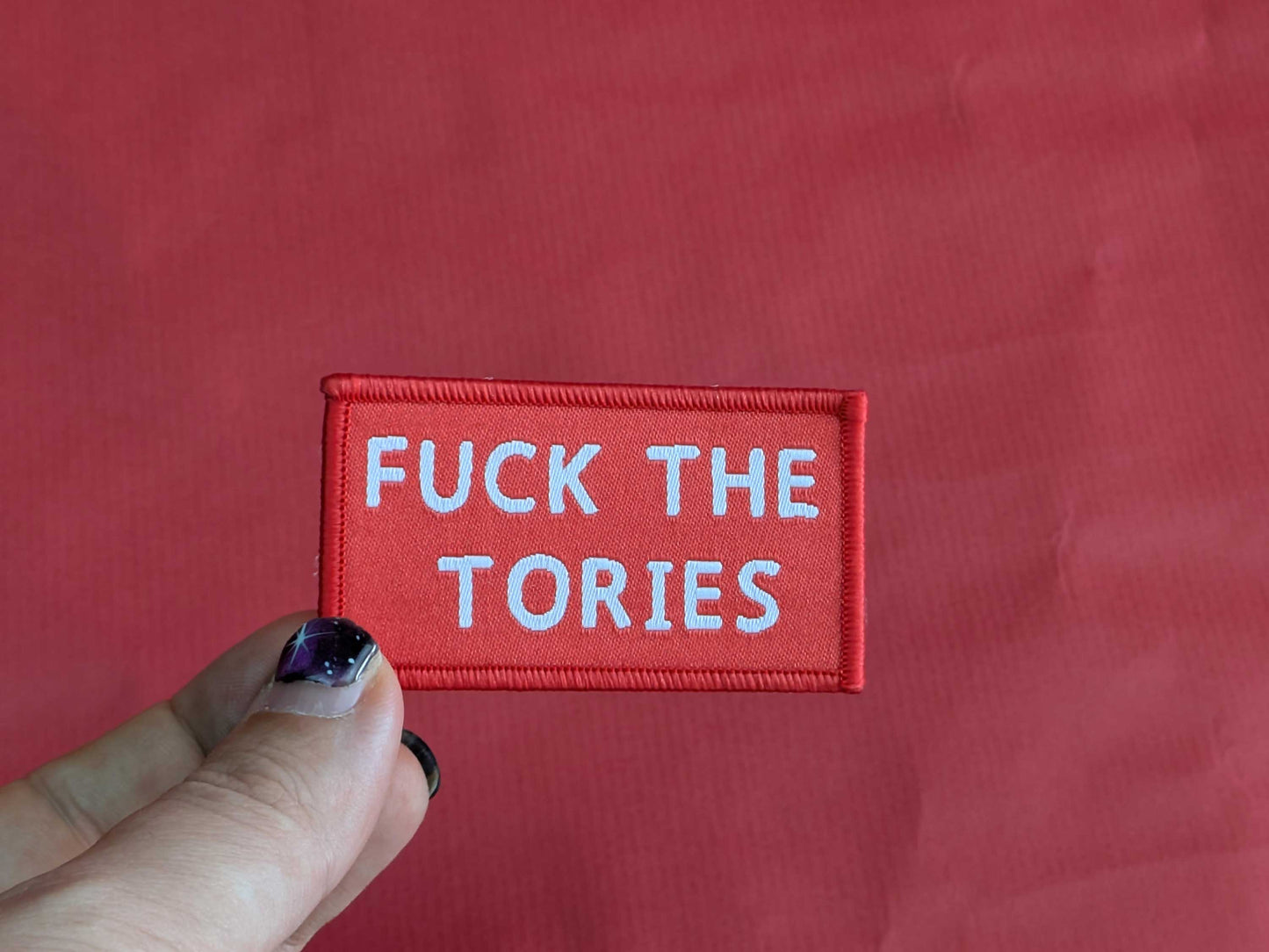 Red patch with white text 'FUCK THE TORIES' held against a red background