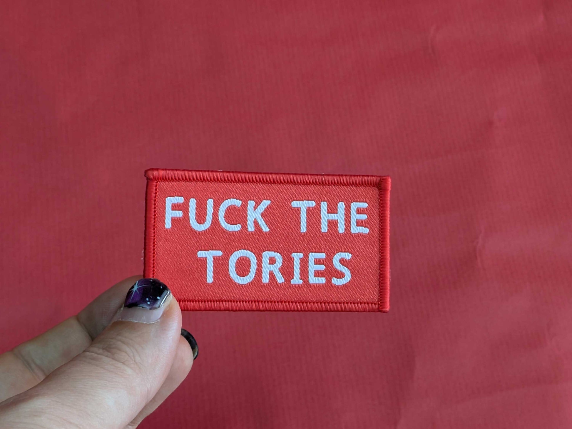 Red patch with white text 'FUCK THE TORIES' held against a red background