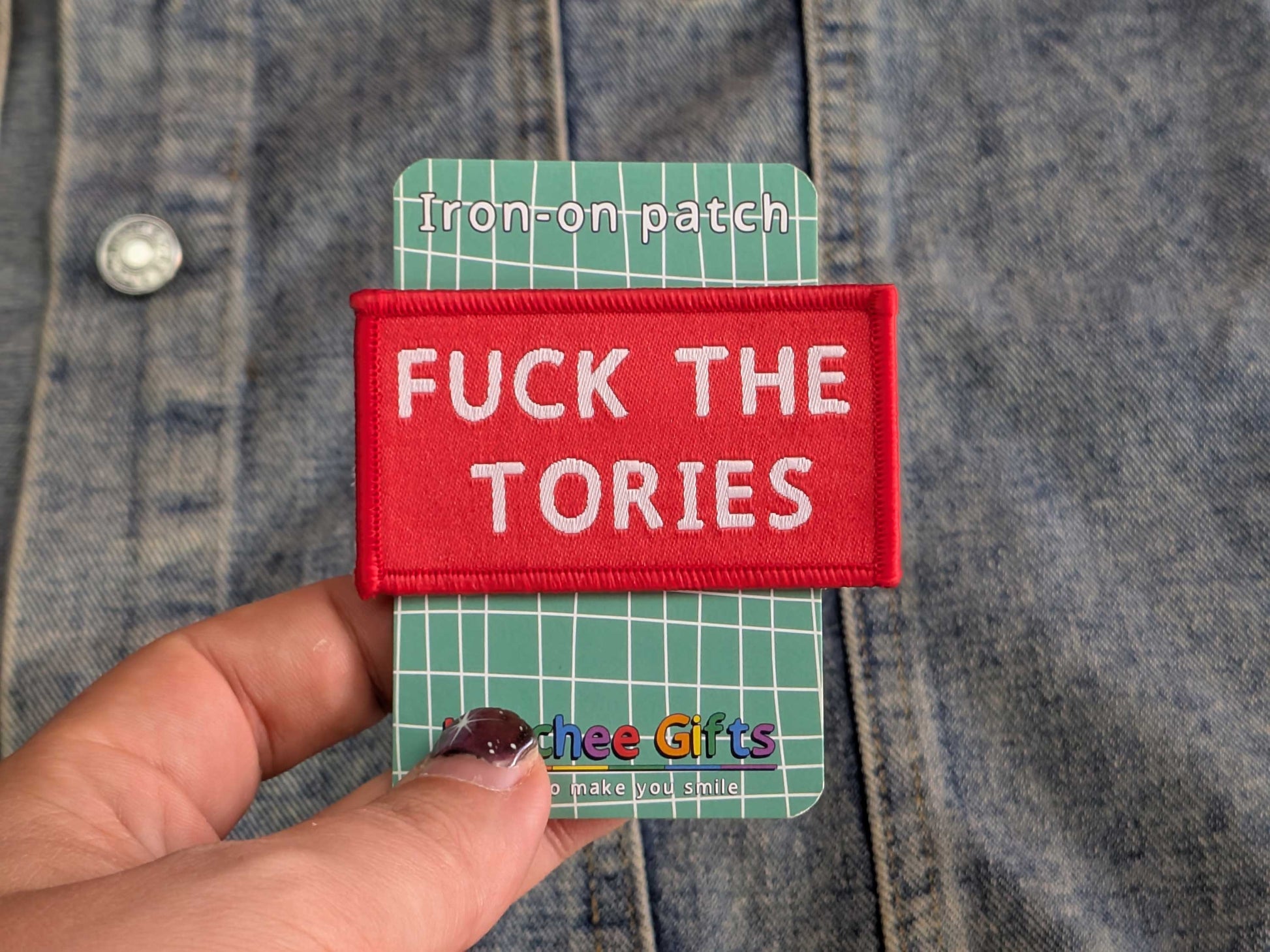 Red iron-on patch with 'FUCK THE TORIES' text held over a denim background