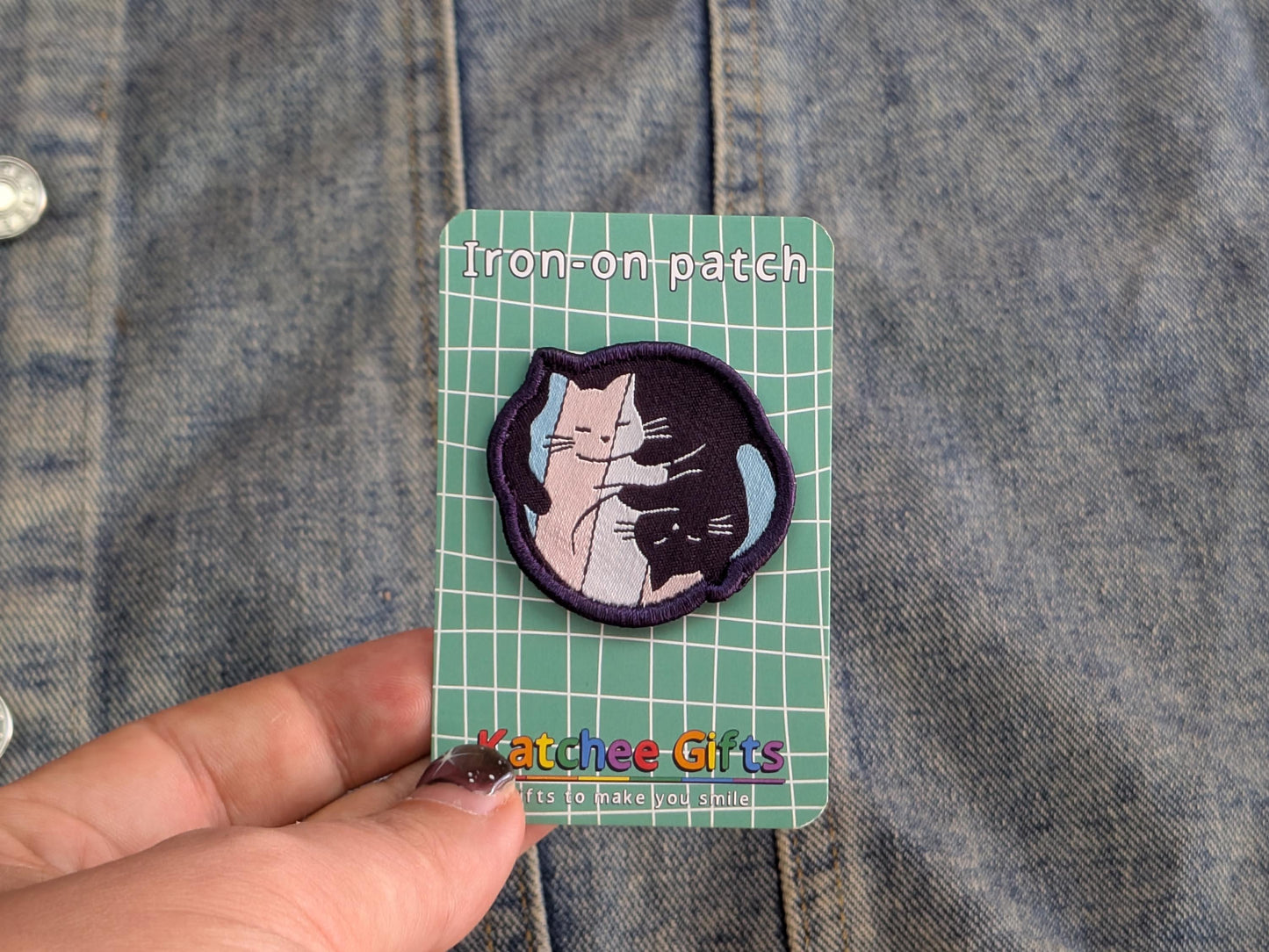 Iron-on patch with a cat design held over a denim background