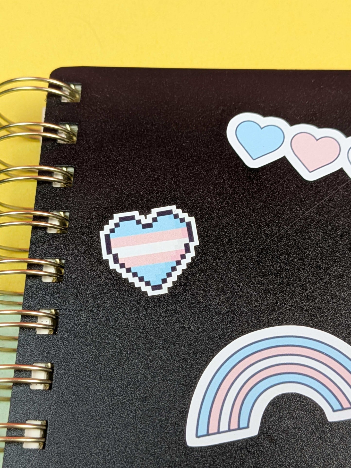 Black notebook with pixelated heart and rainbow stickers on a yellow background
