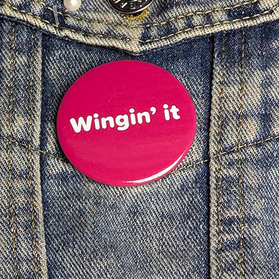 Pink button with 'Wingin' it' text on a denim jacket