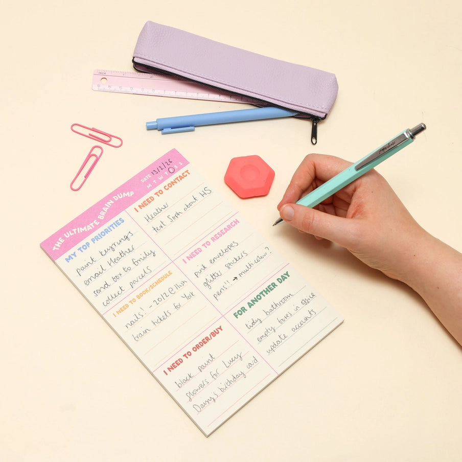 Person holding a pen over a to-do list with stationery items on a beige background