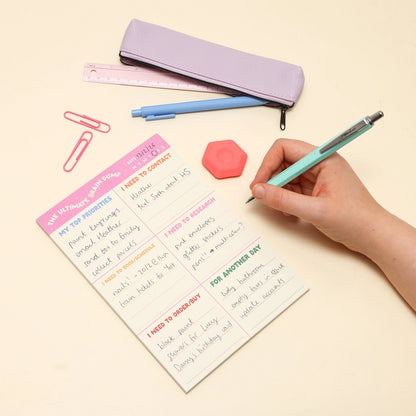 Person holding a pen over a to-do list with stationery items on a beige background