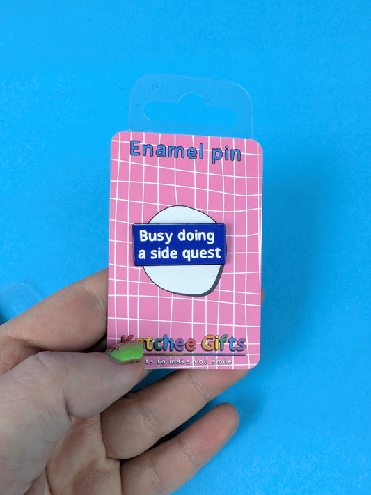 Enamel pin on a pink card held against a blue background