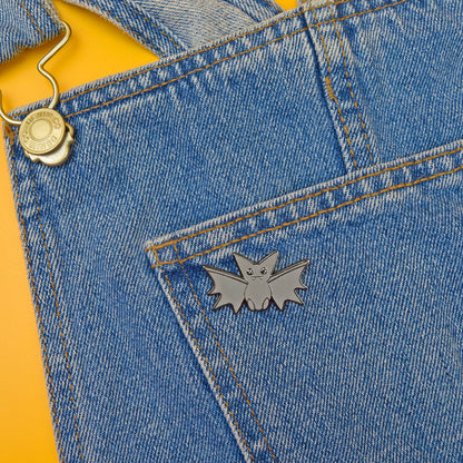 Bat-shaped pin on a blue denim fabric with a yellow background