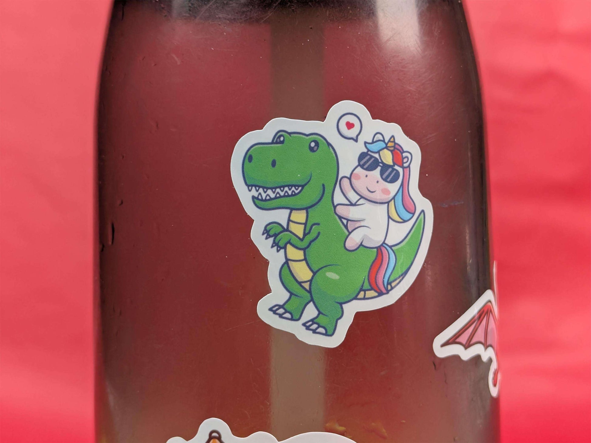 Bottle with a green dinosaur and unicorn sticker on a red background
