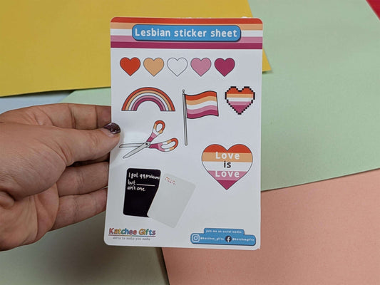 Hand holding a sticker sheet with LGBTQ+ symbols and 'Love is Love' text.