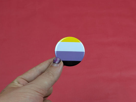 Hand holding a circular badge with a non binary flag design against a red background
