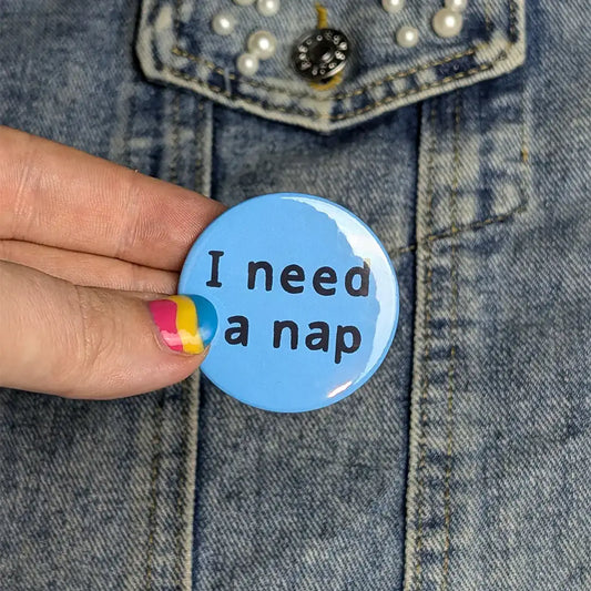 Blue button with 'I need a nap' text held by a hand against a denim background