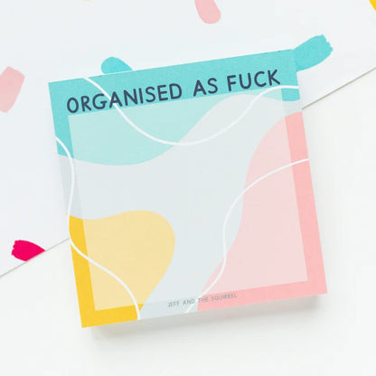 A square greeting card with a bold, humorous design featuring the text 'ORGANISED AS FUCK' in navy blue on a teal band at the top. The card features abstract, fluid color blocks in pastel teal, pink, yellow, and white, framed by a thin white border.