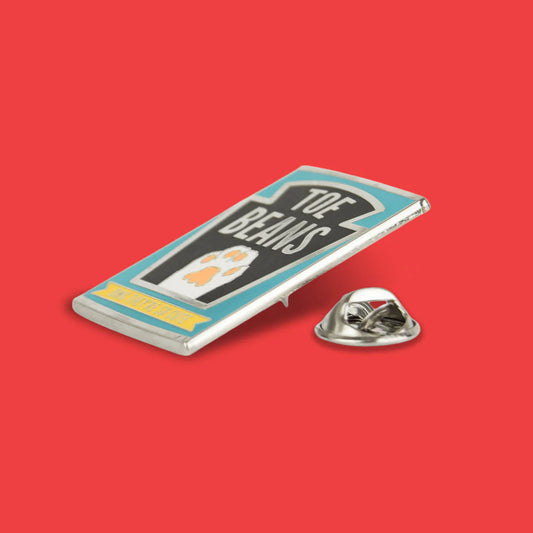 Metallic pin with 'Toe Beans' design on a red background