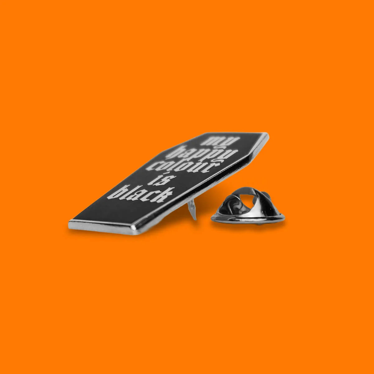 A black enamel lapel pin with silver metal borders and white text reading 'my happy color is black', shown next to its silver metal pin backing on a solid orange background.