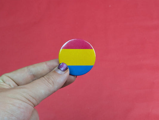 Hand holding a circular badge with a pansexual flag design against a red background