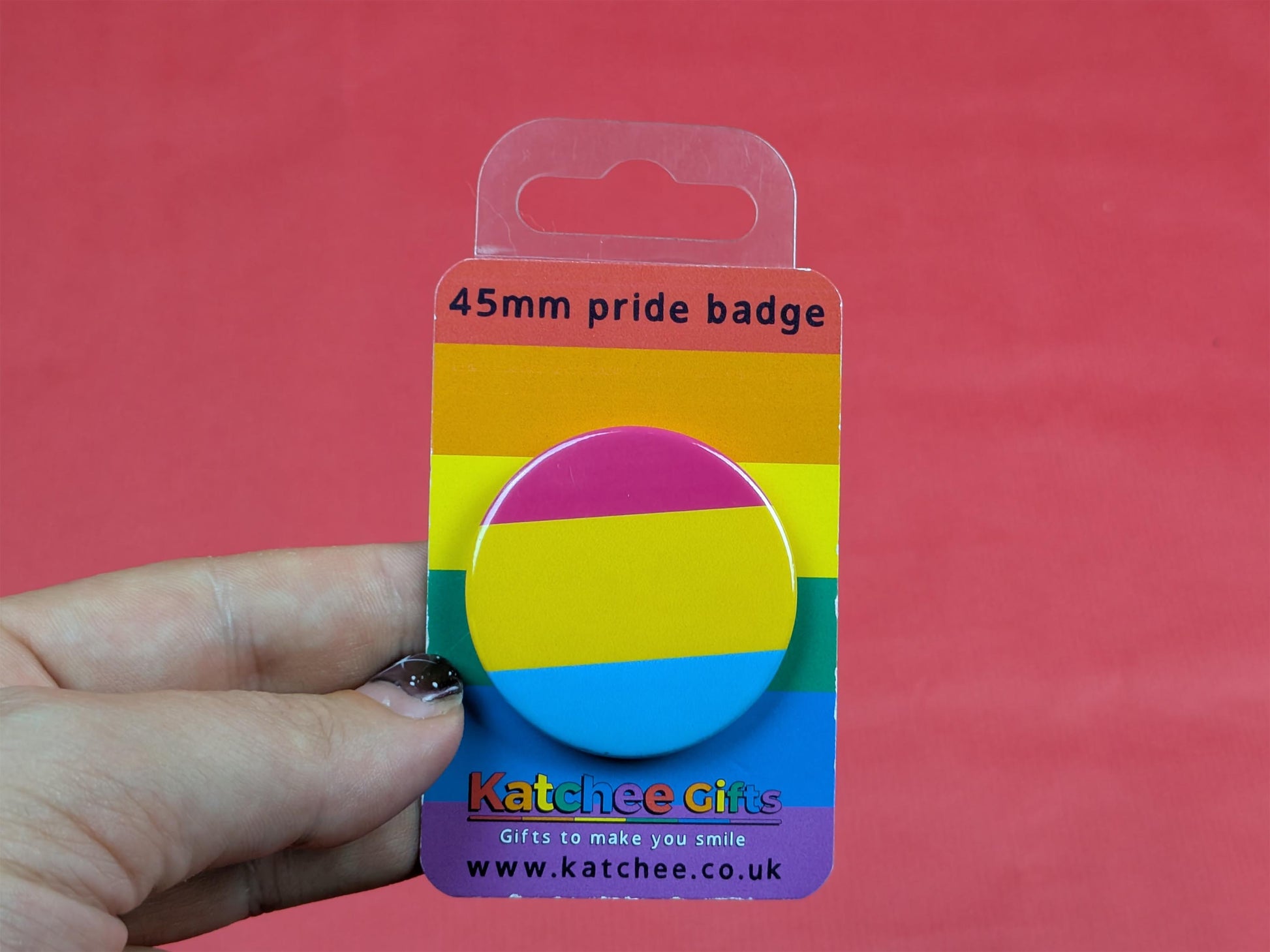 pansexual flag badge in packaging held by a hand against a red background