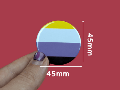 Round badge with a non binary flag design held by a hand against a red background, with measurements indicated.