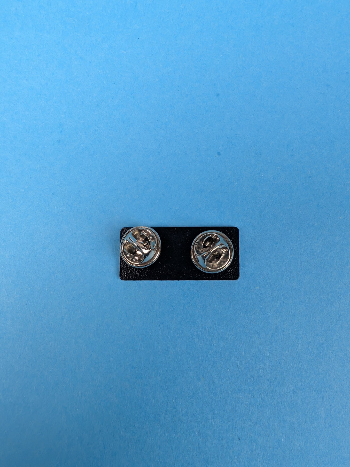 back of enamel pin with butterfly clasps against a blue background