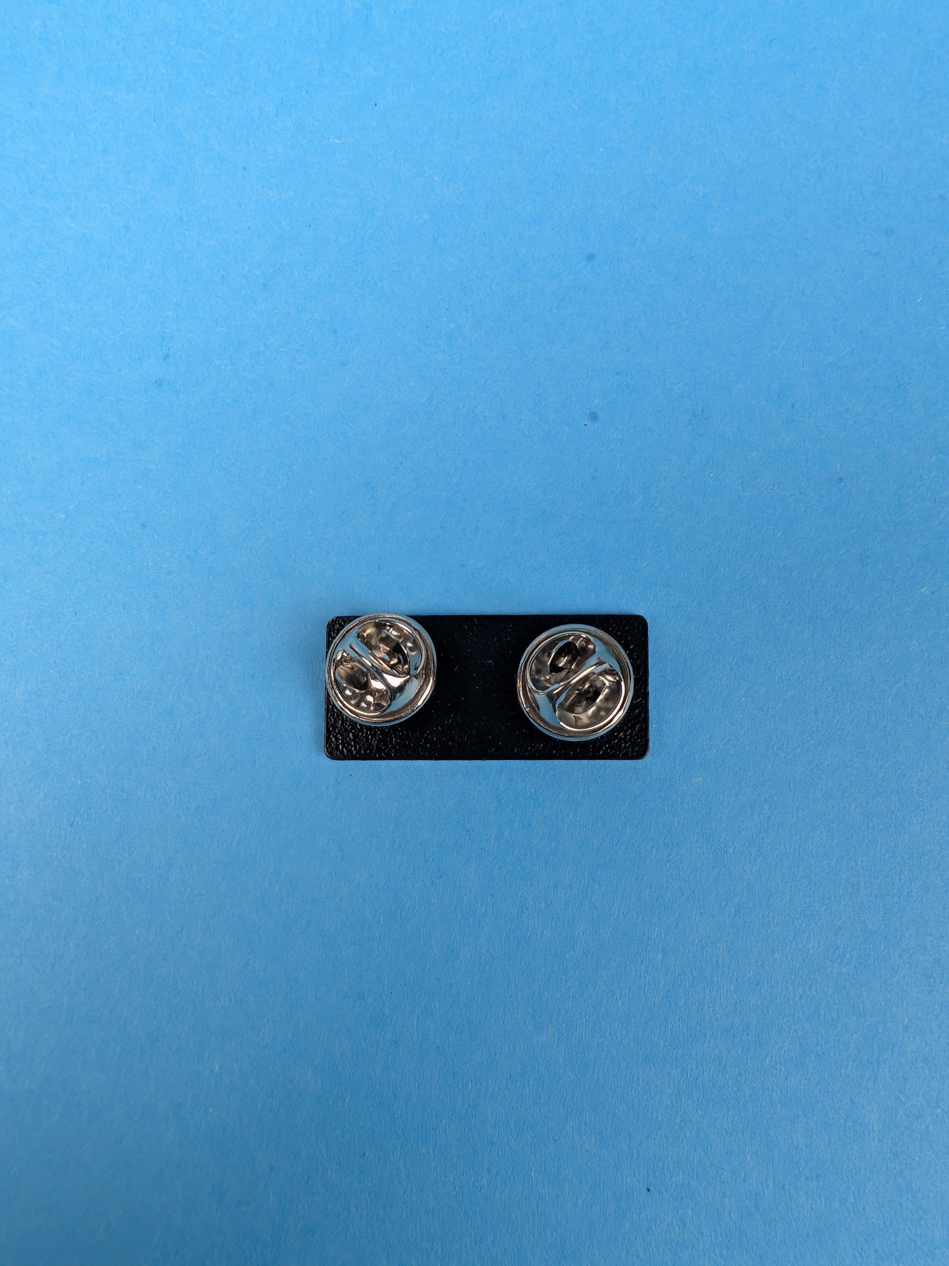 back of enamel pin with butterfly clasps against a blue background