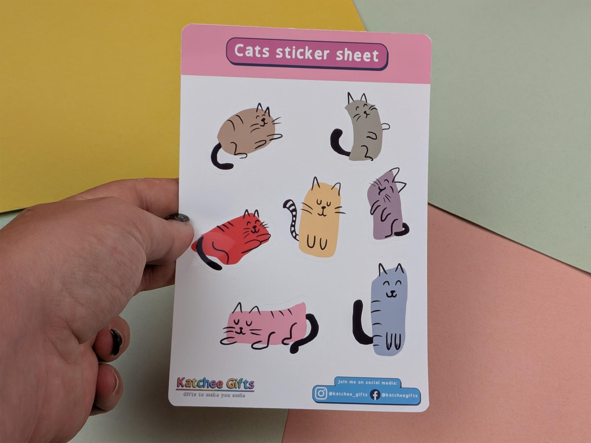 Sheet of cat stickers held by a hand against a colourful background