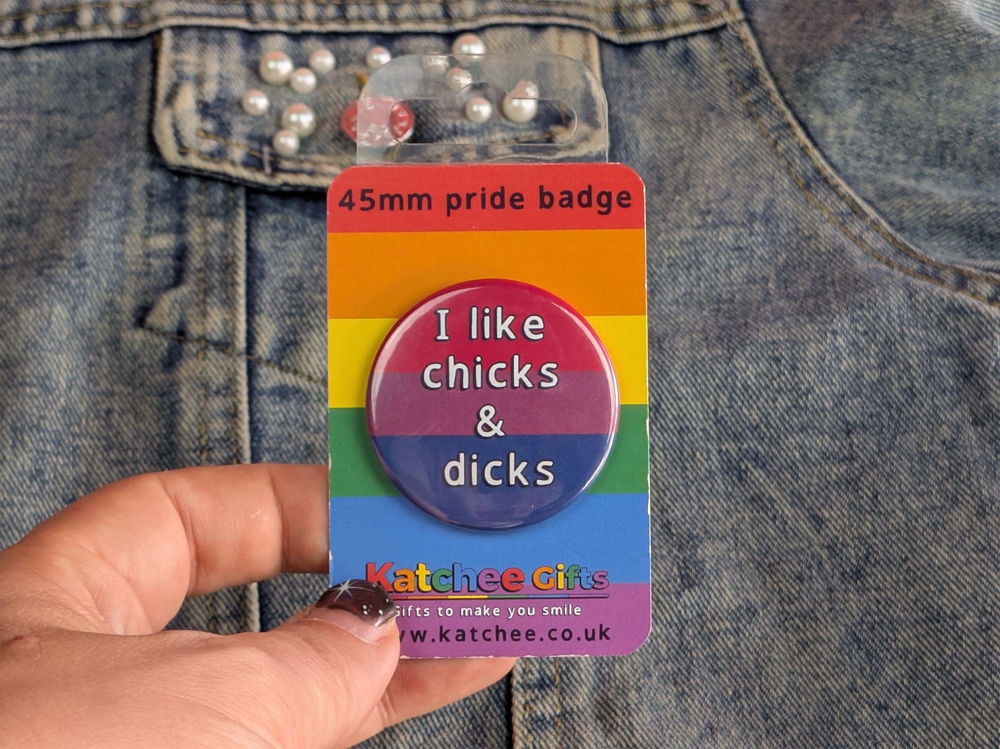 Rainbow pride badge with text 'I like chicks & dicks' held against a denim background