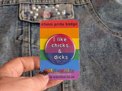 Rainbow pride badge with text 'I like chicks & dicks' held against a denim background