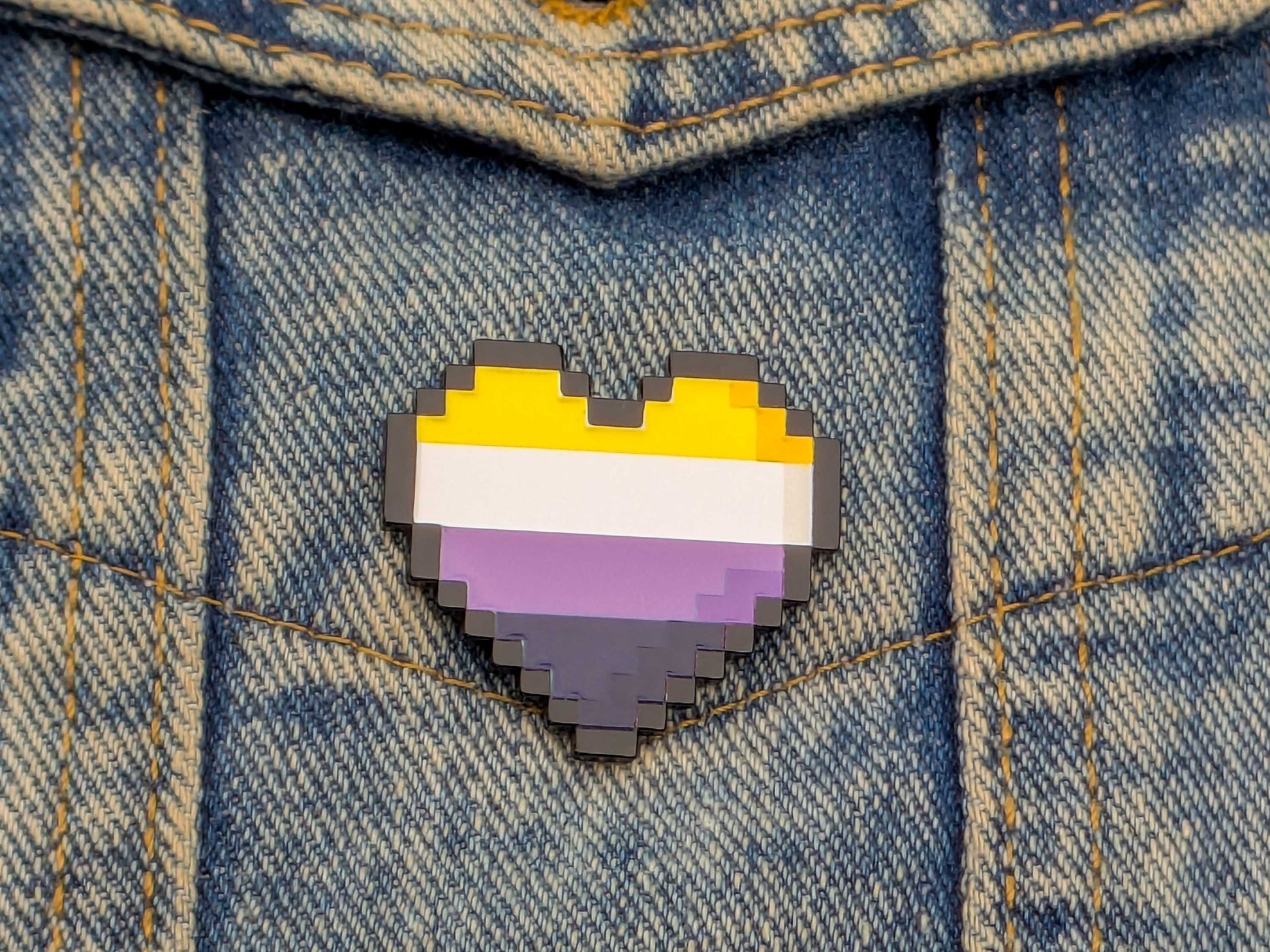 Pixelated heart-shaped pin with a non binary flag design on denim fabric