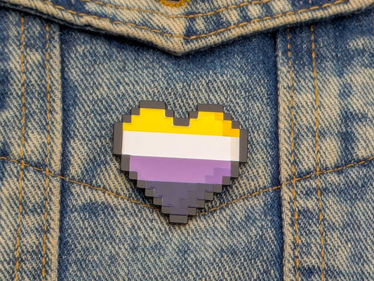 Pixelated heart-shaped pin with a non binary flag design on denim fabric