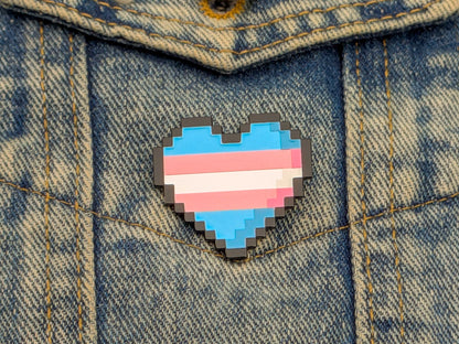 Pixelated heart-shaped pin with a transgender flag design on a denim jacket.